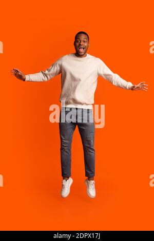 Excited Black Guy Jumping In Air Over Orange Background, Having Fun Stock Photo