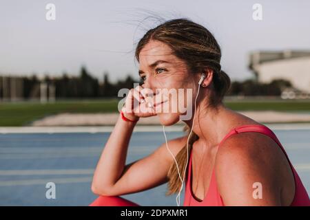 Thoughtful Female Athlete Listening Music While Sitting On Sports Track