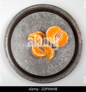 Peeled tangerine fruit, Mandarin pieces on a metal plate and a white background Stock Photo