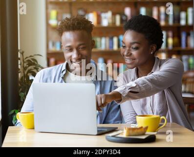 Beauiful black woman pointing at laptop screen, showing something to her boyfriend in coffee shop Stock Photo