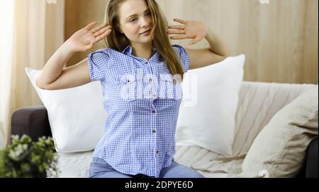 Happy blond woman put hands behind head sitting leaned on couch caucasian female enjoy lazy weekend or vacation in sunny living room Stock Photo