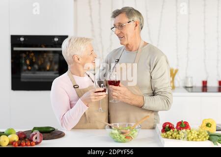 Senior Couple Drinking Wine Celebrating Family Holiday Standing In Kitchen Stock Photo