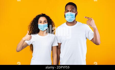 Couple Wearing Face Masks Gesturing Thumbs-Up Standing Over Yellow Background Stock Photo