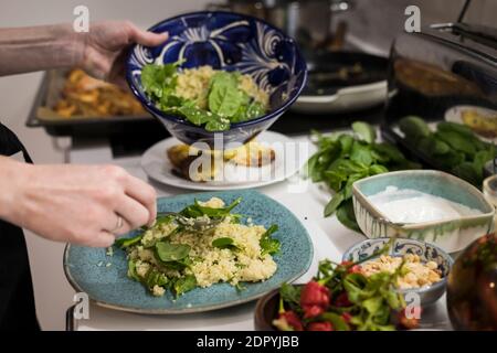 Close up of woman hands garnishing a fresh vegetarian salad with cous cous. Woman cooking in the kitchen at home preparing healthy food. Mediterranean Stock Photo
