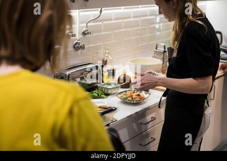 Young charming Swedish woman cooking at home in her kitchen, preparing healthy mediterranean food for her family. Young food blogger doing food prepar Stock Photo