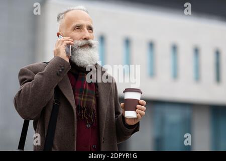 Wealthy senior man with coffee to go having business call Stock Photo