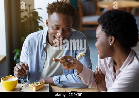 Romantic Valentine's dinner. Loving black couple eating cake together at cafe, spending cozy moments with each oher Stock Photo