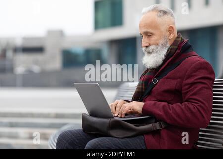 Senior businessman with laptop sitting on bench, working Stock Photo