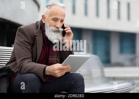 Senior man looking at digital tablet and talking on phone Stock Photo