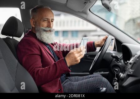 Elderly man driving new car, using mobile phone Stock Photo