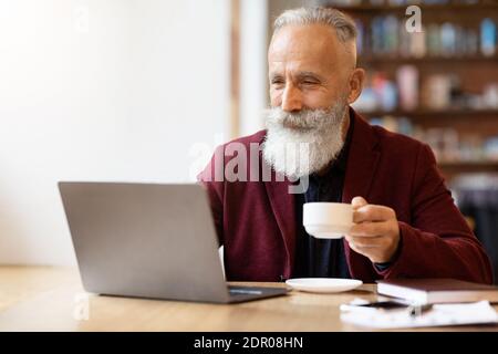 Positive senior man drinking coffee and using laptop Stock Photo
