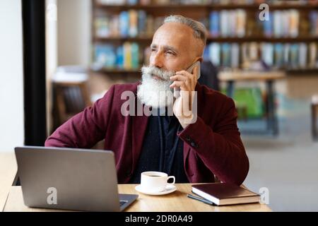 Busy senior businessman talking on phone at cafe Stock Photo