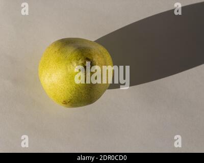 Top view on ripe organic pear lying on white paper and casting dark shadow under sunlight Stock Photo