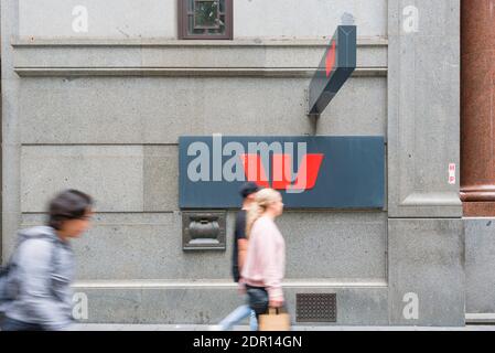 A Westpac Bank symbol at footpath height with blurred people walking past, outside a Sydney city bank branch in Australia Stock Photo