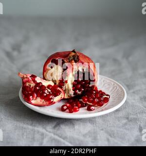 Still life with broken open pomegranate and seeds on plate on table covered with crumpled gray tablecloth Stock Photo