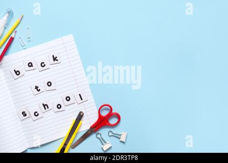 Text Back to School on a lot of sheets of paper on notebook with different school stationery on blue background Stock Photo