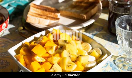 Large plate of fresh exotic fruits for breakfast, mango, bananas, golden kiwi on a table with toasted bread Stock Photo