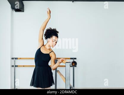 Young Woman Practicing Ballet By Railing In Studio