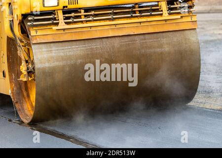Steam billows up from hot asphalt being rolled during road paving work