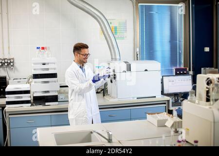 Handsome young researcher workin with chemical samples in laboratory with HPLC system and  chromatography equipment Stock Photo