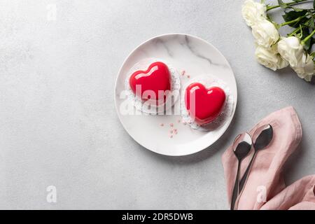 red hearts mousse cakes and bouquet of white roses on gray background Stock Photo