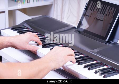 Man hands playing the piano and watching video tutorial on digital tablet computer at home Stock Photo