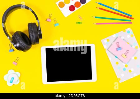 Top view to tablet computer, headphones and school supplies on yellow background. Online learning, education background Stock Photo