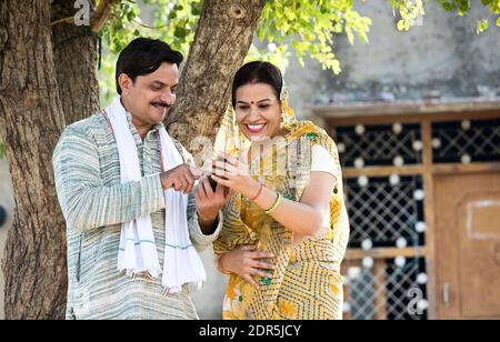Rural Indian wife looking at her husband texting on mobile phone at village Stock Photo