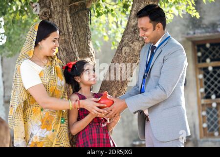 Rural mother and daughter receiving piggy bank from businessman Stock Photo