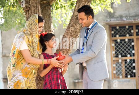 Rural mother and daughter receiving piggy bank from businessman Stock Photo