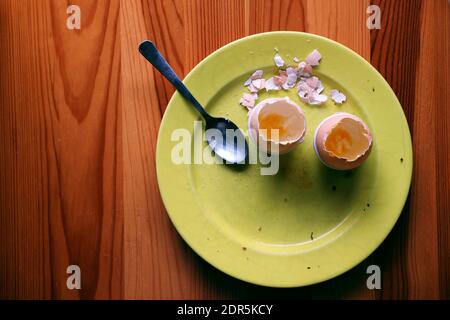 After breakfast - yellow plate with cracked, empty eggshells and a spoon left on a wooden table after a meal Stock Photo