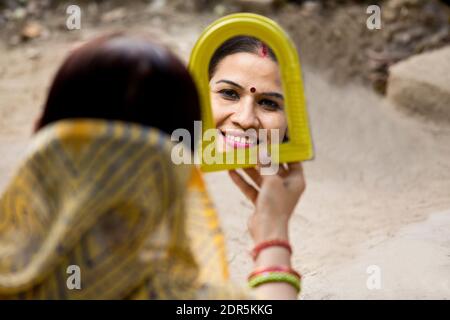 Rural woman looking into mirror in front of her house Stock Photo