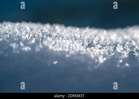 Selective focus on sunlit snow heap with snowflake crystals with blurred blue winter background Stock Photo