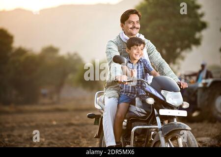 Happy rural Indian farmer with son riding on motorcycle Stock Photo