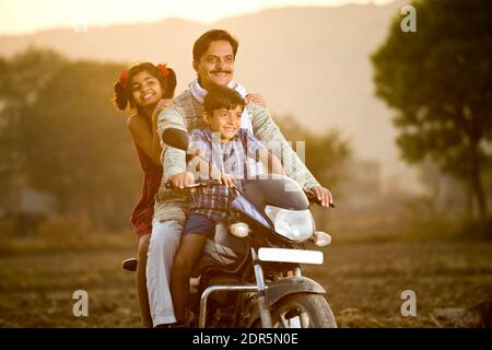 Happy rural Indian farmer with children riding on motorcycle Stock Photo