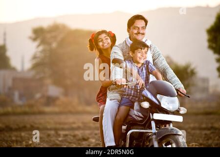 Happy rural Indian farmer with children riding on motorcycle Stock Photo