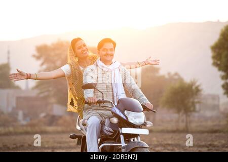 Happy rural Indian couple riding on motorcycle in village Stock Photo