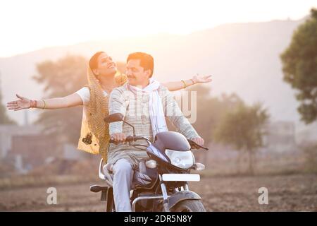 Happy rural Indian couple riding on motorcycle in village Stock Photo