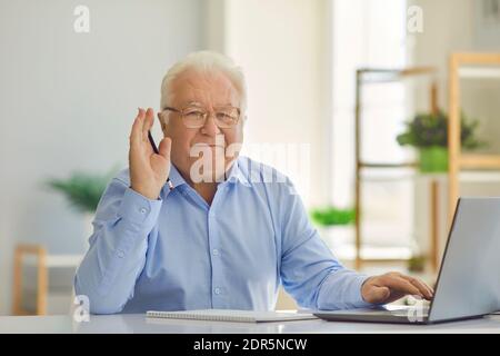 Positive senior man in shirt sitting with notebook and laptop, learning or working online Stock Photo