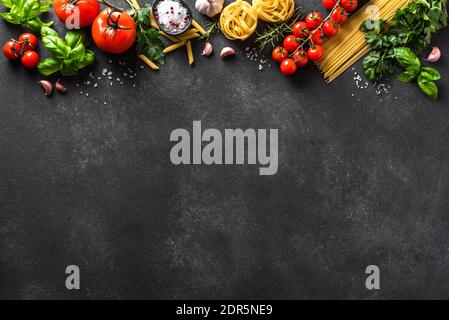 Uncooked pasta and vegetables cooking background, top view, copy space. Various italian pasta, tomatoes, basil herbs and spices, italian cuisine conce Stock Photo
