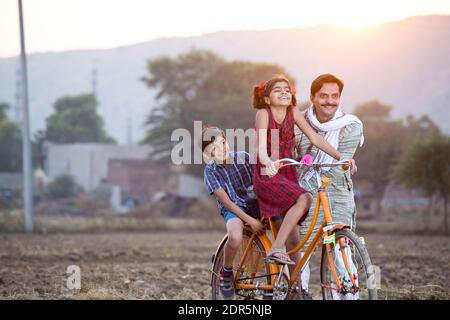 Happy rural Indian farmer with children riding on bicycle Stock Photo