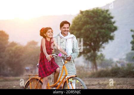 Happy rural Indian farmer with daughter riding on bicycle Stock Photo