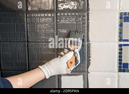 Repainting old dated kitchen ceramic tile back wall with modern gray chalk paint indoors at home. Giving old kitchen new look concept. Hand holding a Stock Photo