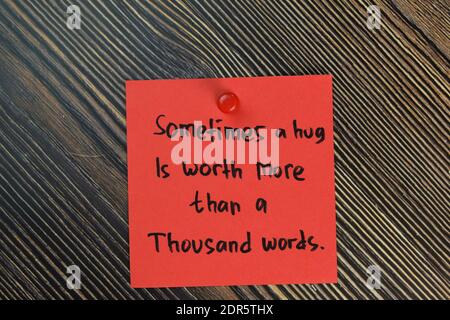 Sometimes a hug is worth more than a thousand words write on sticky notes isolated on Wooden Table. Motivation concept Stock Photo