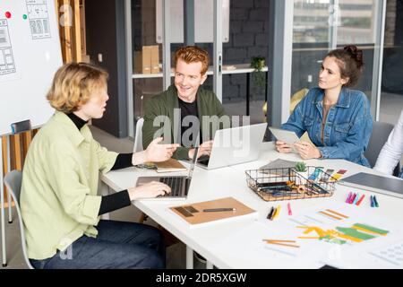 Happy young male mobile app developer looking at one of his female colleagues during brainstorm and discussion of creative ideas Stock Photo