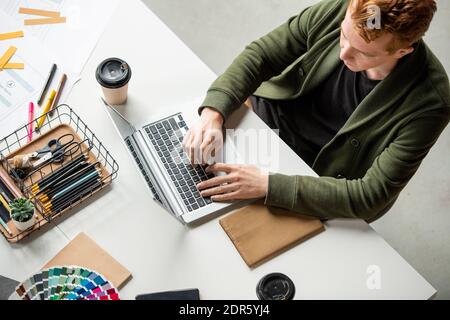 Young contemporary software developer pressing buttons of laptop keypad while looking through examples of new mobile applications Stock Photo