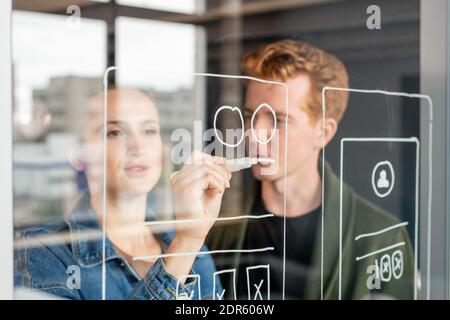 Hand of young female software developer holding white highlighter by transparent noteboard while drawing sketch of mobile application Stock Photo