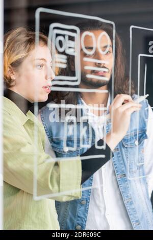Young confident female software developer pointing at sketch of new mobile application while making presentation to male colleague Stock Photo