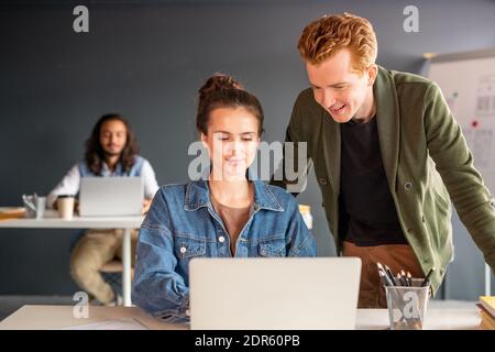 Young confident female designer and her happy male colleague looking at laptop display while preparing presentation of new mobile application Stock Photo