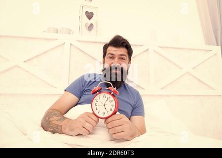 Time to wake up. Healthy habits. Wake up early every morning. Health benefits of rising early. Waking up early gives more time to prepare and be timely. Hipster bearded man in bed with alarm clock. Stock Photo